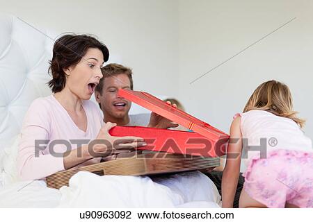 Stock Image - Mother opening presents in bed. Fotosearch