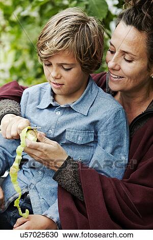 Stock Image - Mother peeling fruit for son outdoors. Fotosearch