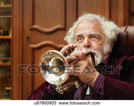 Stock Image - Older man playing trumpet indoors. Fotosearch