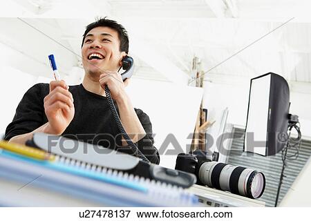 Stock Photo - Photographer talking on phone at desk. Fotosearch