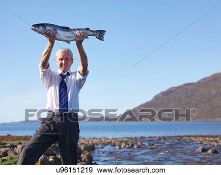 Portrait of businessman holding up freshly caught salmon by loch at fish farm View Large Photo Image Stock Photo - Portrait of businessman holding up freshly caught salmon by loch at fish farm. Fotosearch