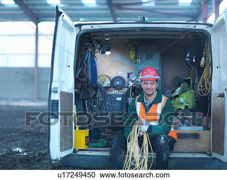 Stock Image - Portrait of construction worker holding cables in back of van on building site. Fotosearch