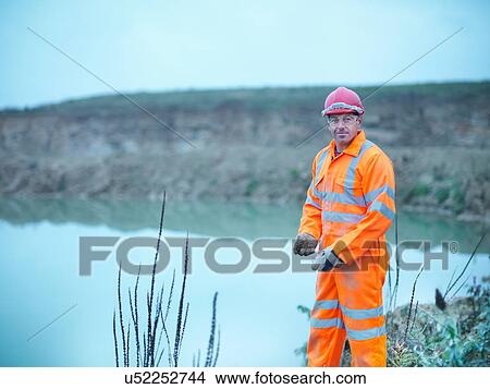 Picture - Portrait of ecologist taking soil samples from bank next to water on quarry site. Fotosearch