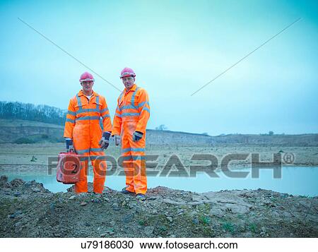 Stock Image - Portrait of ecologists in reflective clothing standing by water at quarry site. Fotosearch