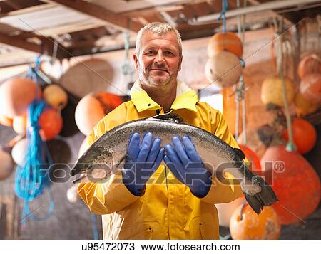 Stock Image - Portrait of fisherman holding freshly caught salmon in hut. Fotosearch