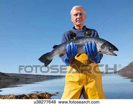Stock Photo - Portrait of fisherman standing in loch holding freshly caught salmon. Fotosearch