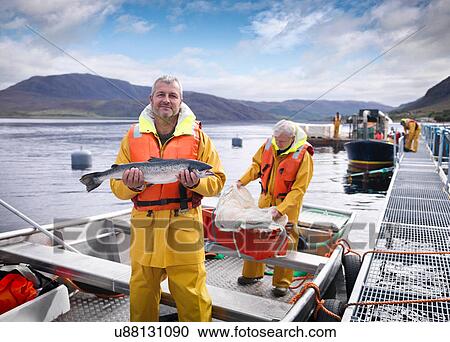 Stock Image - Portrait of fisherman with freshly caught salmon on loch of Scottish salmon farm. Fotosearch