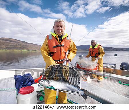 Stock Photo - Portrait of fisherman with freshly caught salmon in net on loch of Scottish salmon farm. Fotosearch