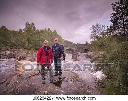Portrait of hikers standing on rocks by flowing river View Large Photo Image Stock Photo - Portrait of hikers standing on rocks by flowing river. Fotosearch