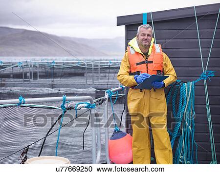 Stock Image - Portrait of salmon farmer with clipboard on Scottish salmon farm pontoon. Fotosearch
