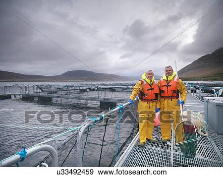 Stock Photo - Portrait of salmon farmers on hand reared Scottish salmon farm on sea loch. Fotosearch