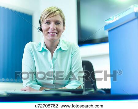 Stock Image - Portrait of telephone receptionist wearing headset at desk. Fotosearch