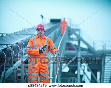 Portrait of workman in reflective clothing holding walkie talkie on steps of screening conveyor at quarry View Large Photo Image Stock Photo - Portrait of workman in reflective clothing holding walkie talkie on steps of screening conveyor at quarry. Fotosearch