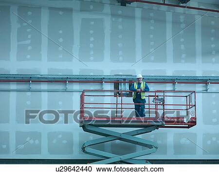 Stock Image - Portrait of workman on scissor lift of building site. Fotosearch
