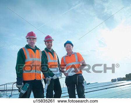 Stock Image - Portrait of workmen and apprentice with tools and plans on factory roof. Fotosearch