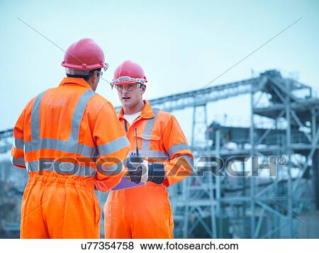 Stock Photo - Quarryman advising apprentice in on site meeting in front of quarry machinery. Fotosearch