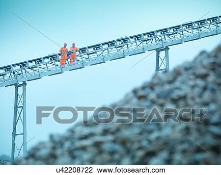 Stock Image - Quarrymen standing on stockpile conveyor at stone quarry. Fotosearch