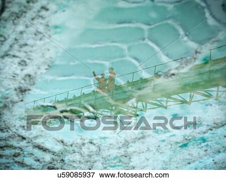 Stock Photo - Reflection in puddle of workmen standing on screening conveyor at stone quarry. Fotosearch