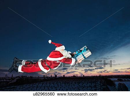 Stock Image - Santa Claus flying with wrapped gift. Fotosearch