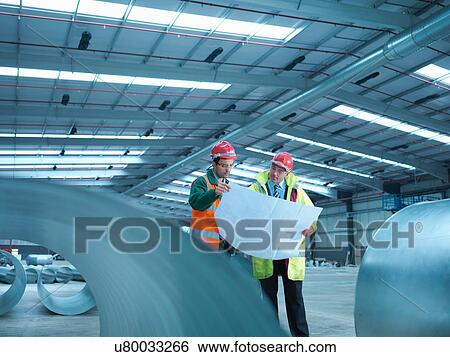 Site foreman advising apprentice with plans in partly completed factory View Large Photo Image Stock Photograph - Site foreman advising apprentice with plans in partly completed factory. Fotosearch