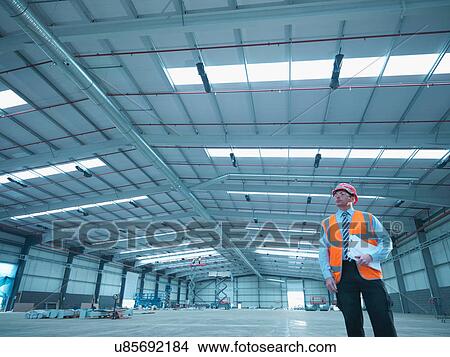 Picture - Site foreman with clipboard in partly completed factory. Fotosearch