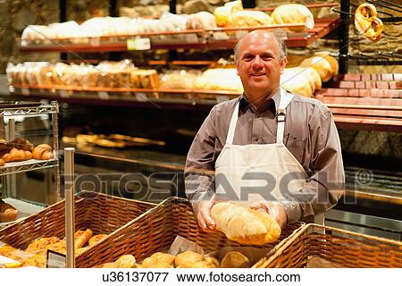 Smiling baker holding loaf of bread View Large Photo Image Stock Photo - Smiling baker holding loaf of bread. Fotosearch
