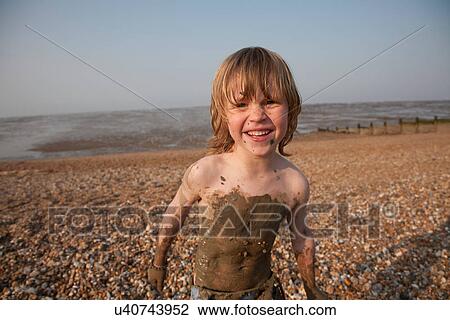 Stock Image - Smiling boy covered in mud at beach. Fotosearch