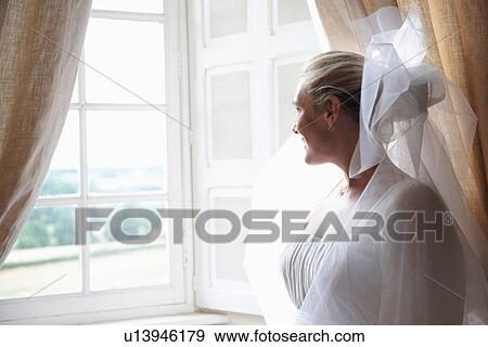 Smiling bride standing near window View Large Photo Image Stock Photo - Smiling bride standing near window. Fotosearch