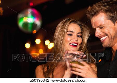 Stock Image - Smiling couple having cocktails in club. Fotosearch