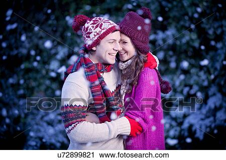 Stock Image - Smiling couple hugging in snow. Fotosearch