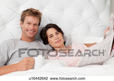Smiling couple reading newspaper in bed View Large Photo Image Stock Image - Smiling couple reading newspaper in bed. Fotosearch