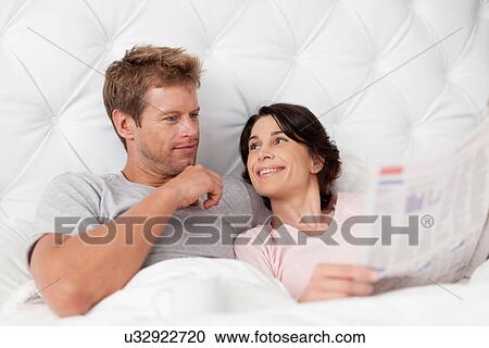 Smiling couple reading newspaper in bed View Large Photo Image Stock Image - Smiling couple reading newspaper in bed. Fotosearch