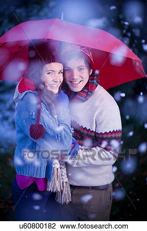 Stock Image - Smiling couple under umbrella in snow. Fotosearch