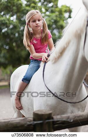 Stock Photo - Smiling girl riding horse in yard. Fotosearch
