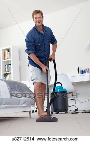 Picture - Smiling man vacuuming living room. Fotosearch
