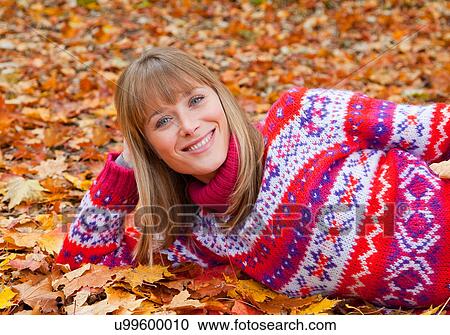 Stock Image - Smiling woman laying in fall leaves. Fotosearch