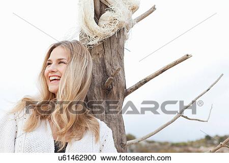 Stock Image - Smiling woman leaning against tree. Fotosearch