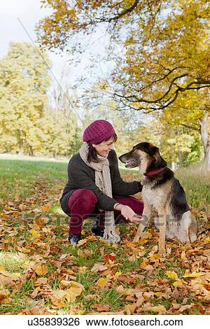 Stock Photograph - Smiling woman petting dog in park. Fotosearch