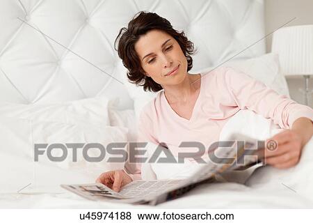 Smiling woman reading newspaper in bed View Large Photo Image Stock Photo - Smiling woman reading newspaper in bed. Fotosearch