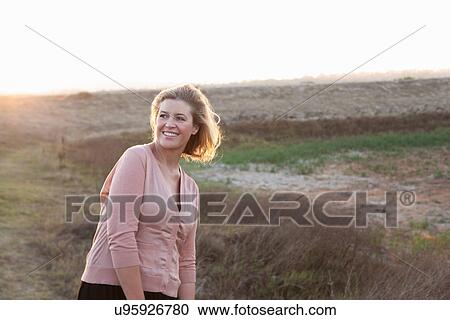 Stock Image - Smiling woman standing in wheat field. Fotosearch
