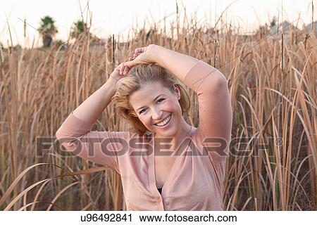 Stock Image - Smiling woman standing in wheat field. Fotosearch