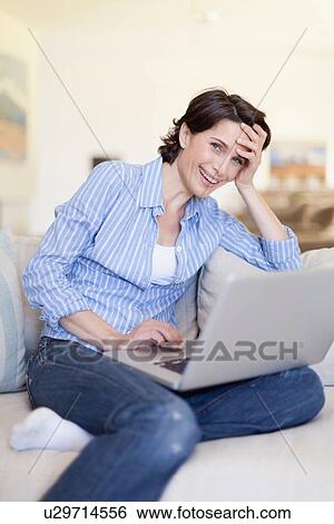 Stock Photograph - Smiling woman using laptop on couch. Fotosearch