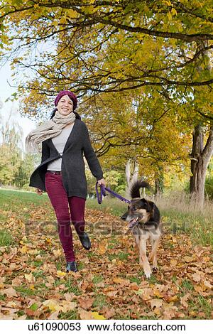 Stock Image - Smiling woman walking dog in park. Fotosearch