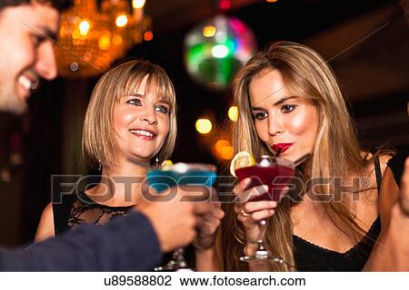 Stock Image - Smiling women having cocktails in club. Fotosearch