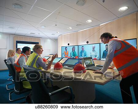 Staff members in meeting room with colleagues on video conference screens View Large Photo Image Stock Photo - Staff members in meeting room with colleagues on video conference screens. Fotosearch