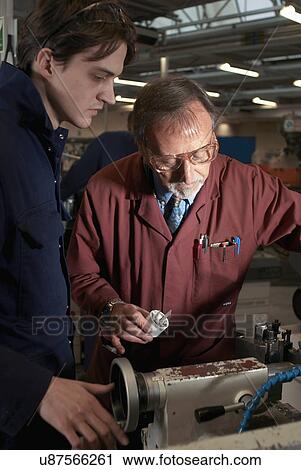 Stock Image - Teacher helping student in shop class. Fotosearch