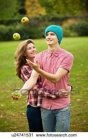 Stock Image - Teenage couple juggling apples in park. Fotosearch