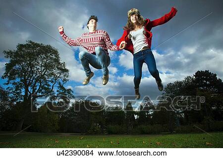 Picture - Teenage couple jumping for joy in park. Fotosearch