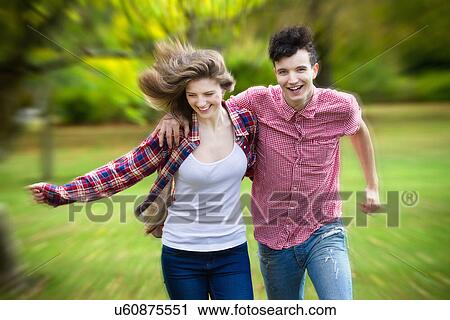 Stock Image - Teenage couple running in park. Fotosearch