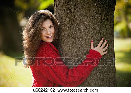Stock Image - Teenage girl hugging tree in park. Fotosearch